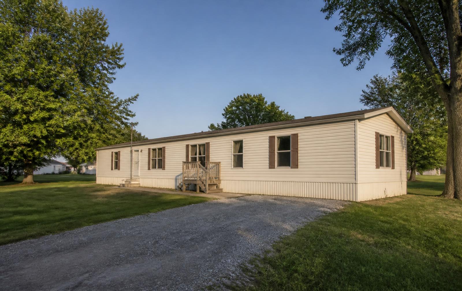 A single-wide manufactured home on a grassy lot in a Midwest small town